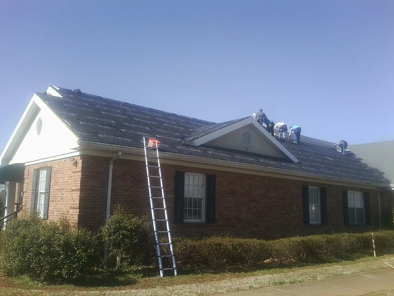 Crew tearing shingles off a brick ranch roof with a ladder set — Metal Roof Repair work by our crew in Watonga