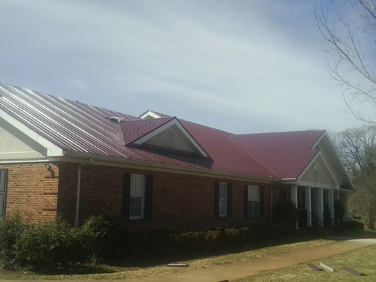 Red metal roof with gabled entries on a long brick building, from a Hail Damage Roof Repair job in Watonga