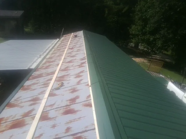 Old rusted panels beside newly installed green metal roofing — Wind Damage Roof Repair by Roofing Brothers in Watonga