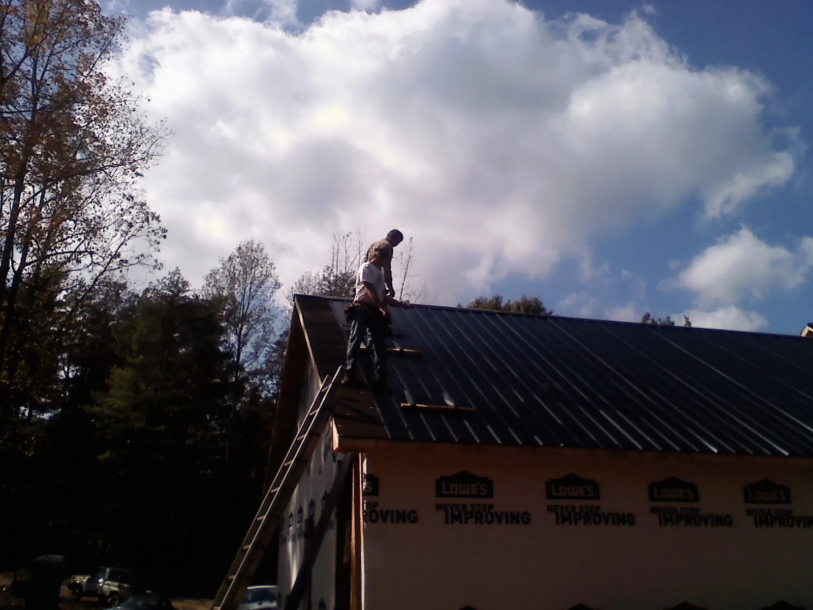Roofer fastening dark metal panels high against a cloudy sky, from a Roof Inspection job in Watonga